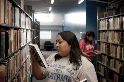 Photo of student in library holding and looking at book.