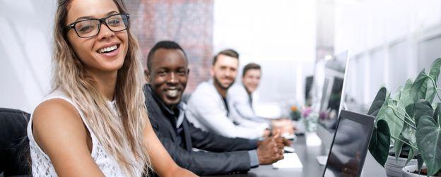 Four people working on laptops smile at the camera